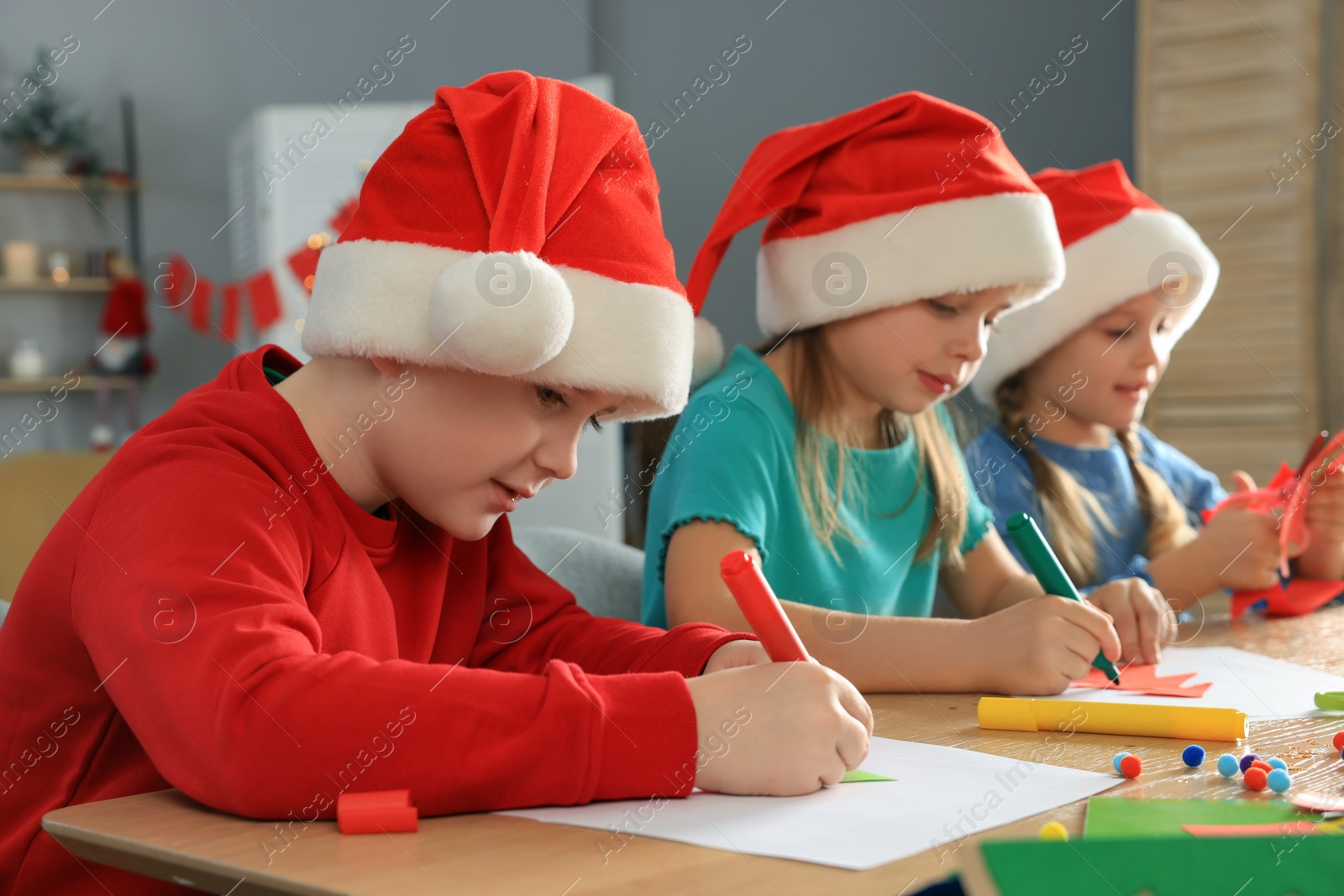 Photo of Cute little children in Santa hats making beautiful Christmas greeting cards at home