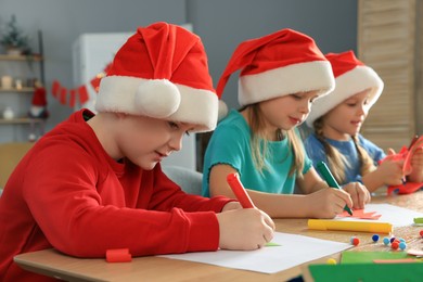 Cute little children in Santa hats making beautiful Christmas greeting cards at home