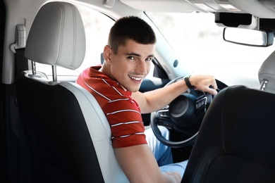 Attractive young man driving luxury car, view from backseat