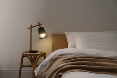 Stylish lamp on table near bed indoors