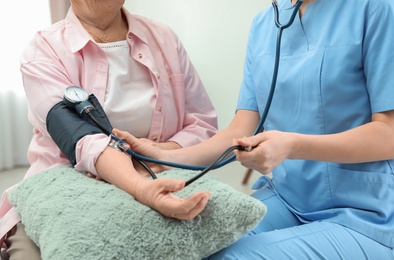 Nurse measuring blood pressure of elderly woman indoors, closeup. Assisting senior people