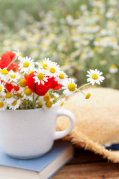 Cup with chamomiles and poppies on wooden table outdoors