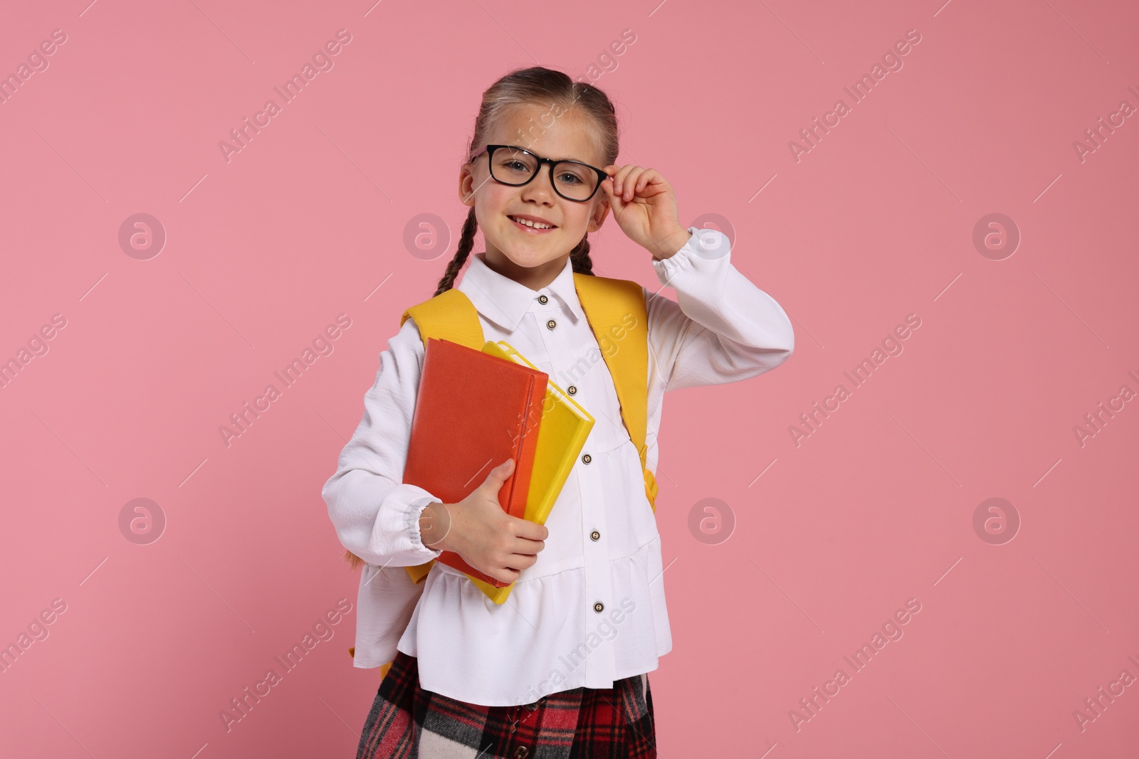 Photo of Happy schoolgirl in glasses with backpack and books on pink background