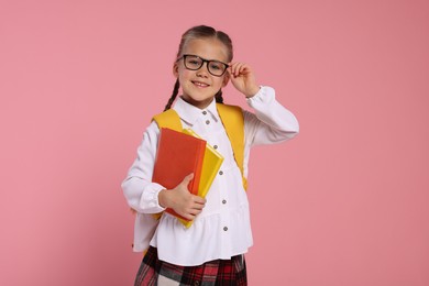 Happy schoolgirl in glasses with backpack and books on pink background