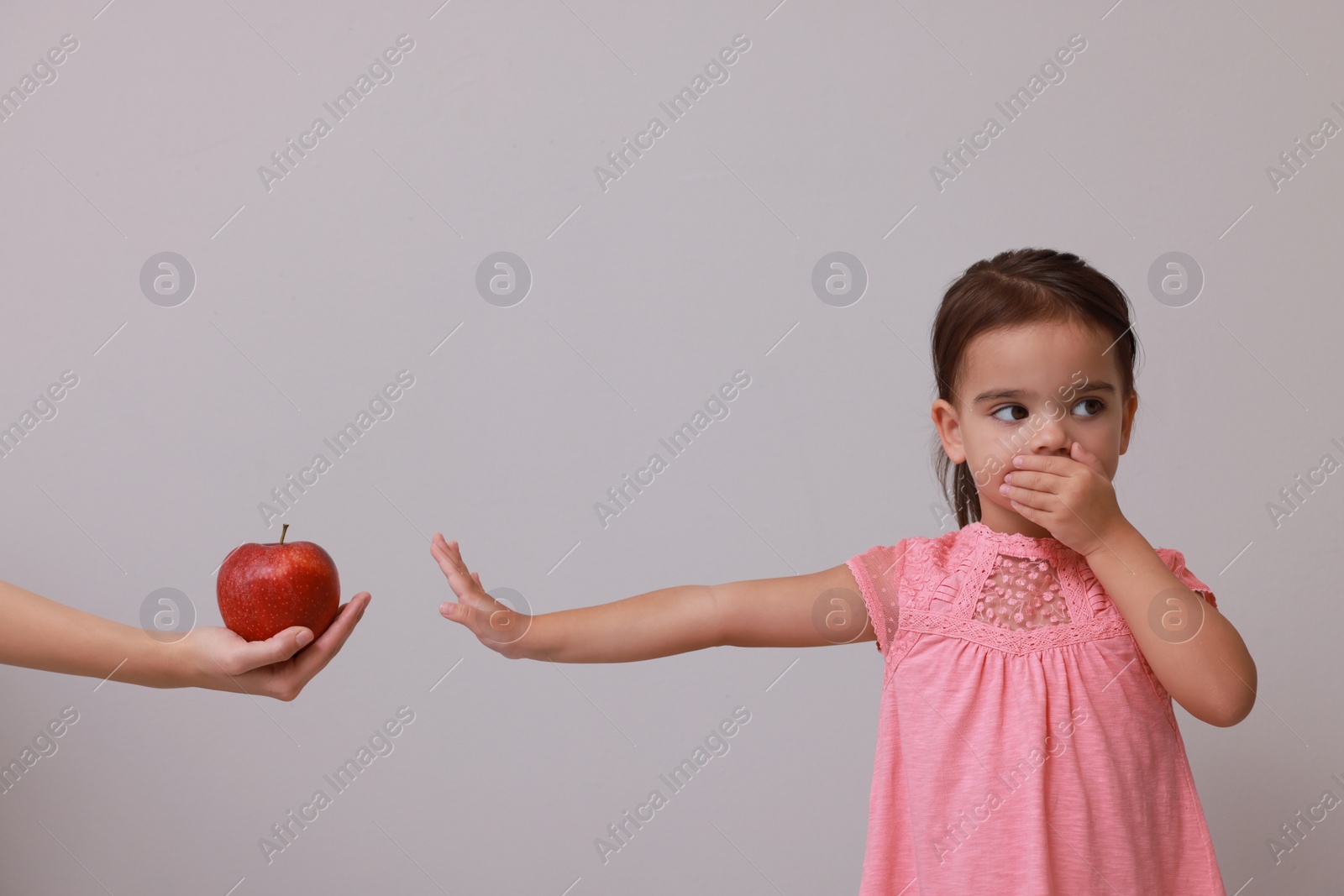 Photo of Cute little girl covering mouth and refusing to eat apple on grey background