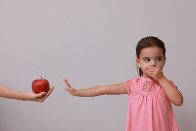 Photo of Cute little girl covering mouth and refusing to eat apple on grey background