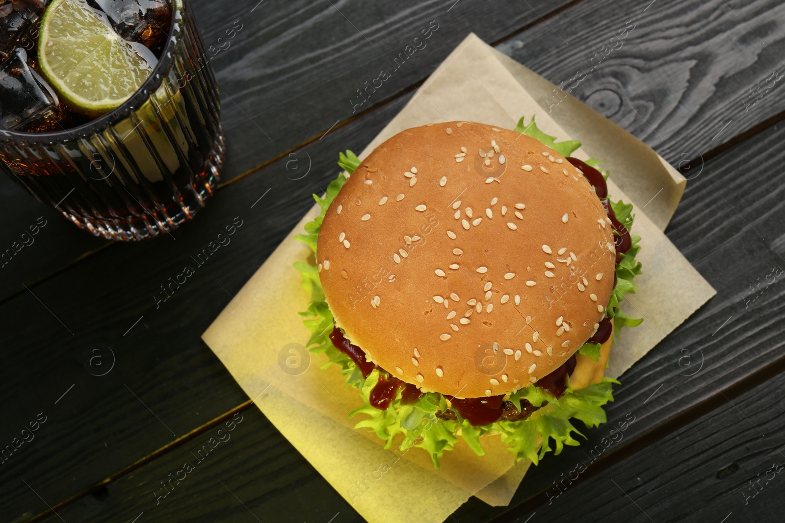 Photo of Burger with delicious patty and soda drink on black wooden table, above view