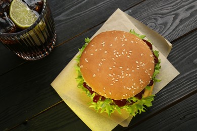 Photo of Burger with delicious patty and soda drink on black wooden table, above view