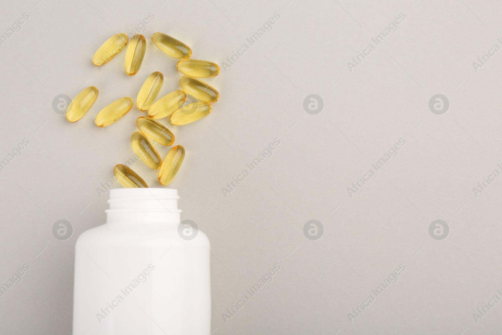 Photo of Bottle and vitamin capsules on light grey background, top view. Space for text