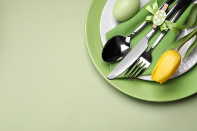 Photo of Festive Easter table setting with egg on light green background, top view. Space for text