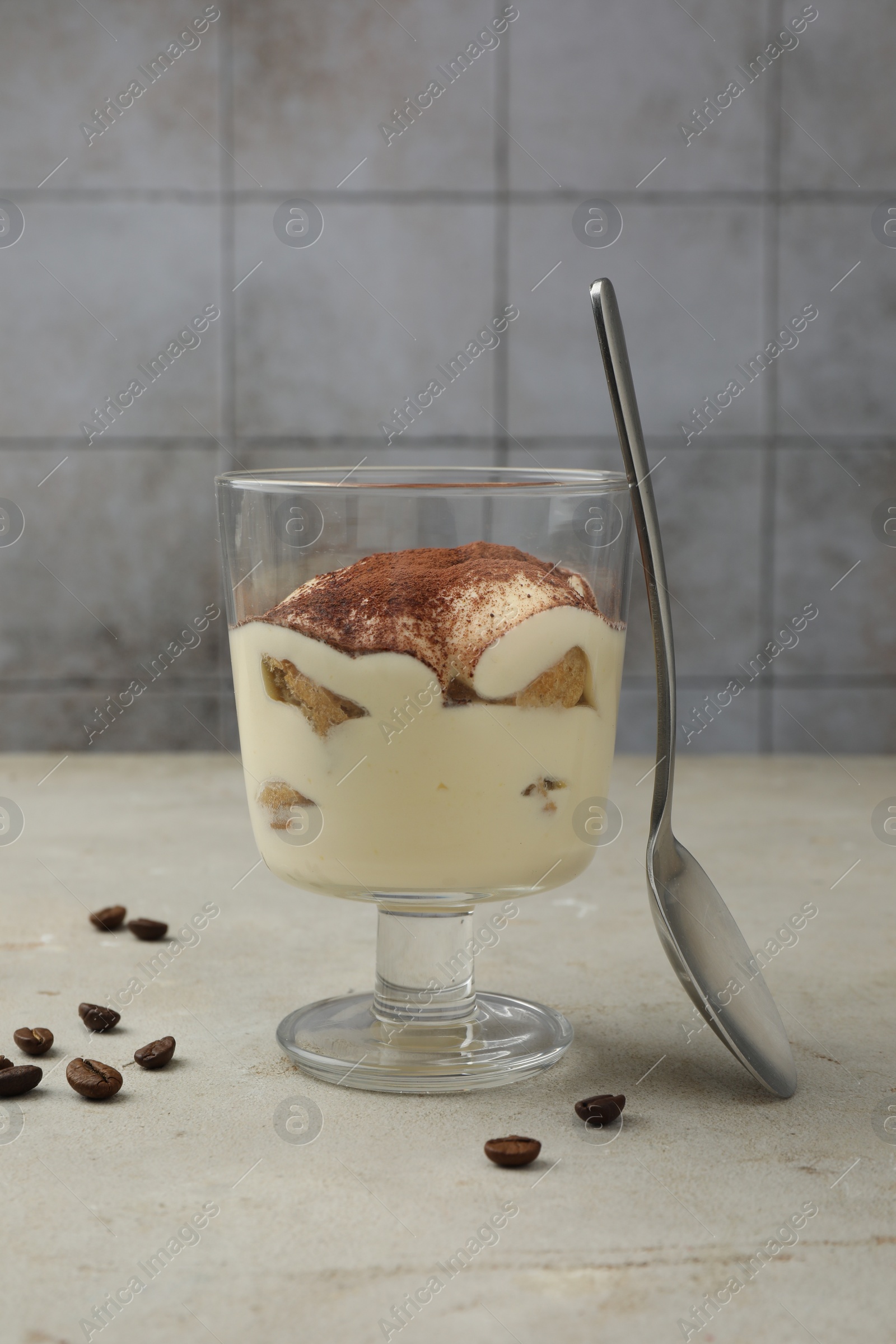 Photo of Delicious tiramisu in glass, spoon and scattered coffee beans on light table