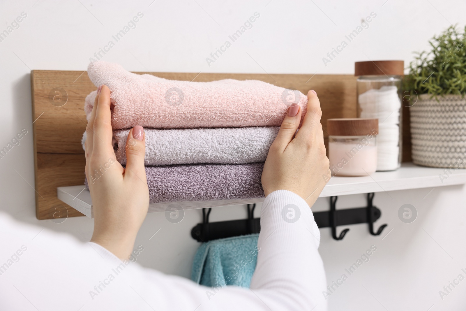 Photo of Woman stacking clean towels on shelf indoors, closeup