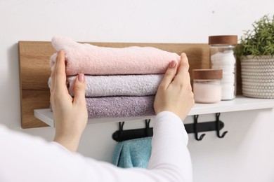 Photo of Woman stacking clean towels on shelf indoors, closeup