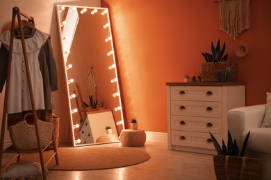 Large mirror with light bulbs and chest of drawers in stylish room interior