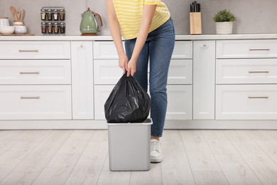 Photo of Woman taking garbage bag out of trash bin in kitchen, closeup