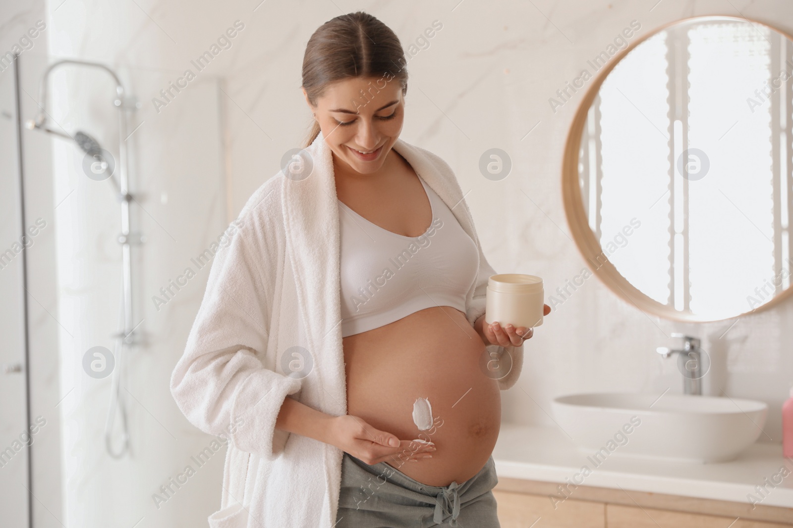 Photo of Young pregnant woman with cosmetic product in bathroom