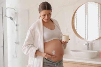 Young pregnant woman with cosmetic product in bathroom