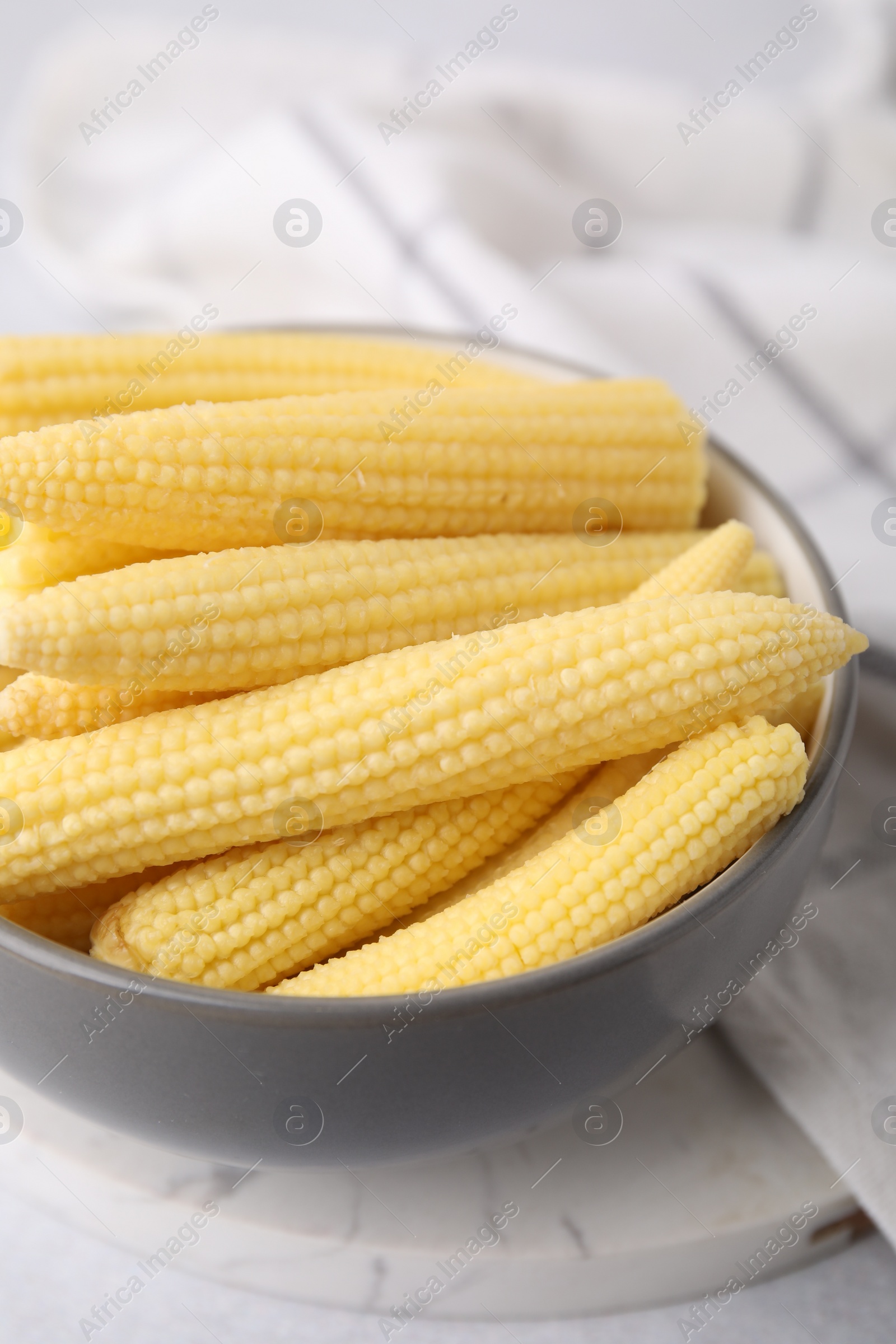 Photo of Tasty fresh yellow baby corns in bowl on white table, closeup