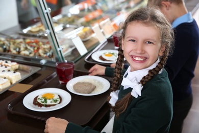 Photo of Cute girl near serving line with healthy food in school canteen