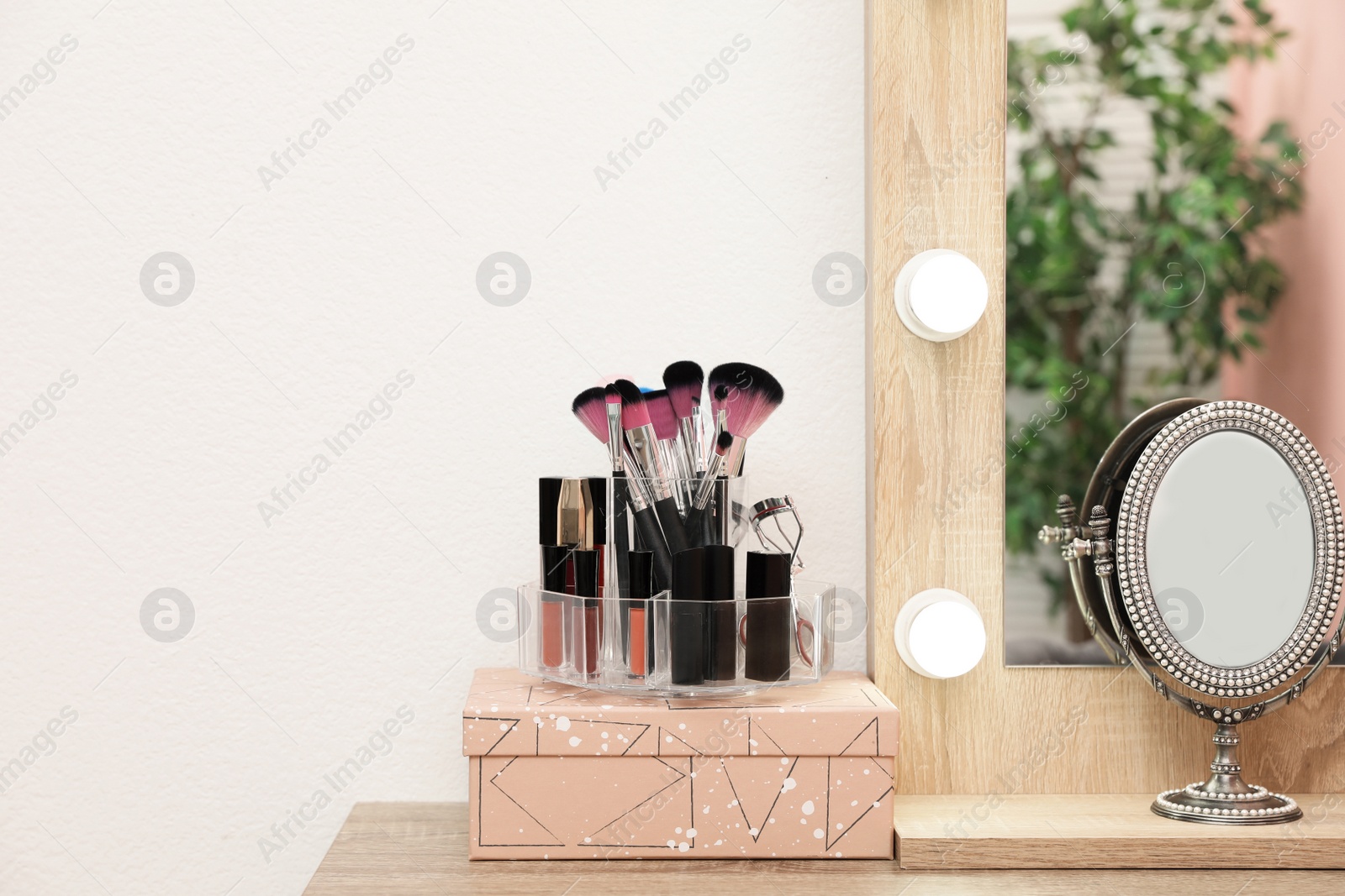 Photo of Organizer with cosmetic products for makeup on table near mirror. Space for text