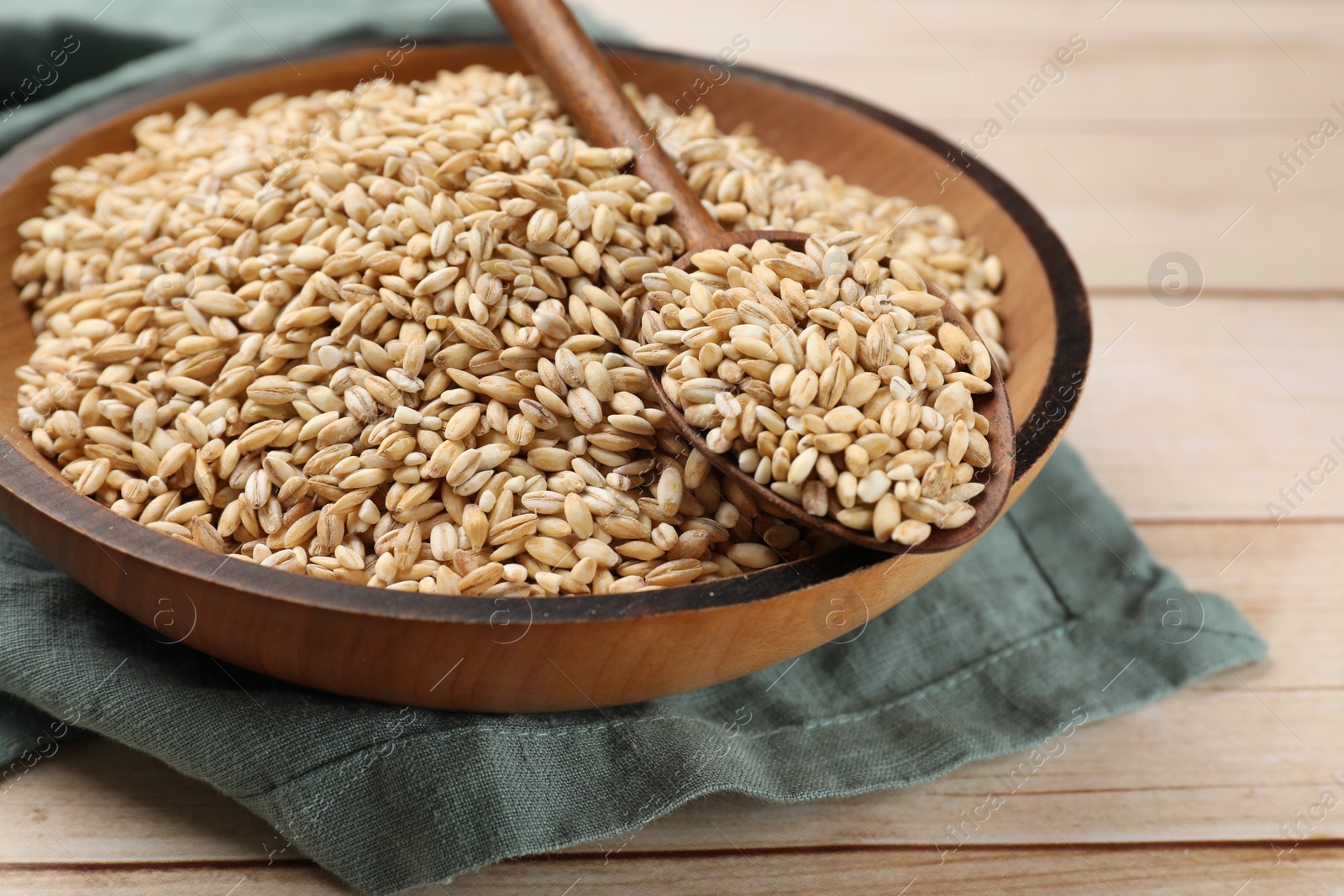 Photo of Dry pearl barley in bowl and spoon on light wooden table, closeup