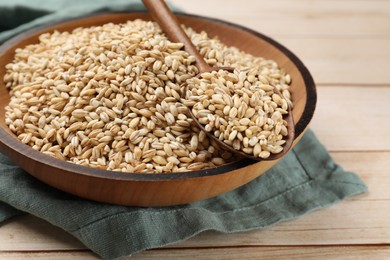 Dry pearl barley in bowl and spoon on light wooden table, closeup