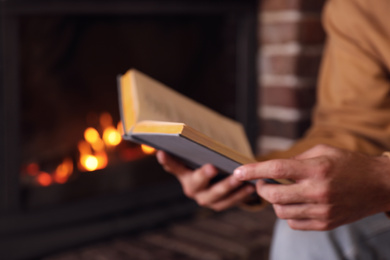 Man reading book near fireplace at home, closeup