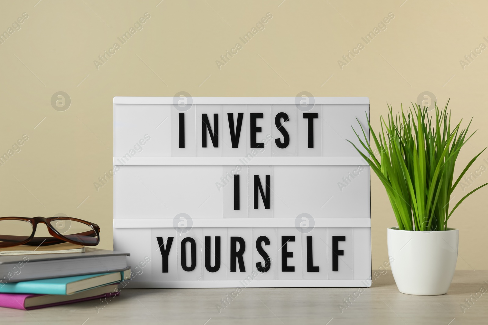 Photo of Lightbox with motivational quote Invest in Yourself, stationery and plant on white wooden table