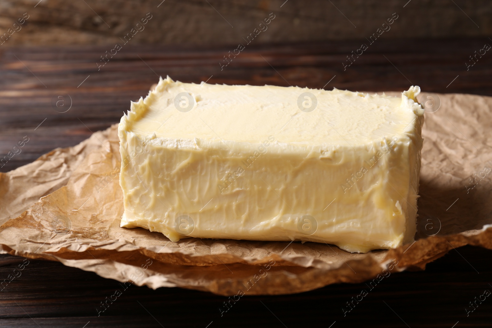 Photo of Parchment with piece of tasty homemade butter on wooden table, closeup