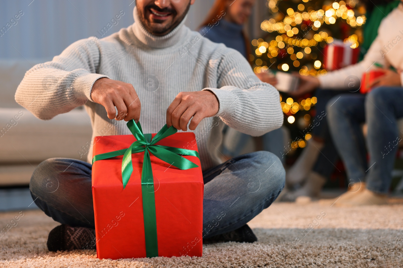 Photo of Christmas celebration in circle of friends. Happy man opening gift at home, selective focus