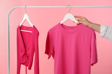 Photo of Woman taking stylish t-shirt from rack on pink background, closeup
