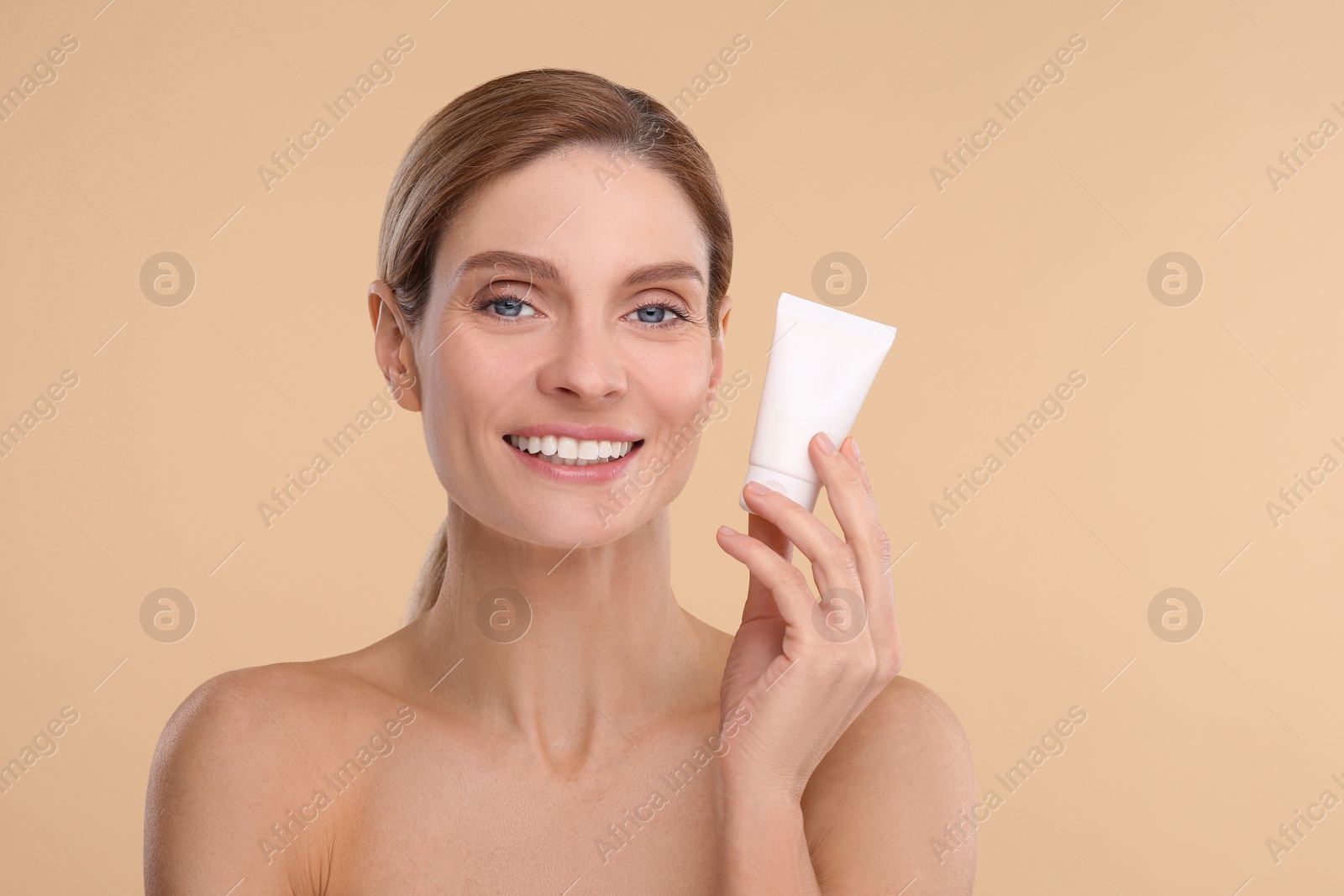 Photo of Woman holding tube of foundation on beige background