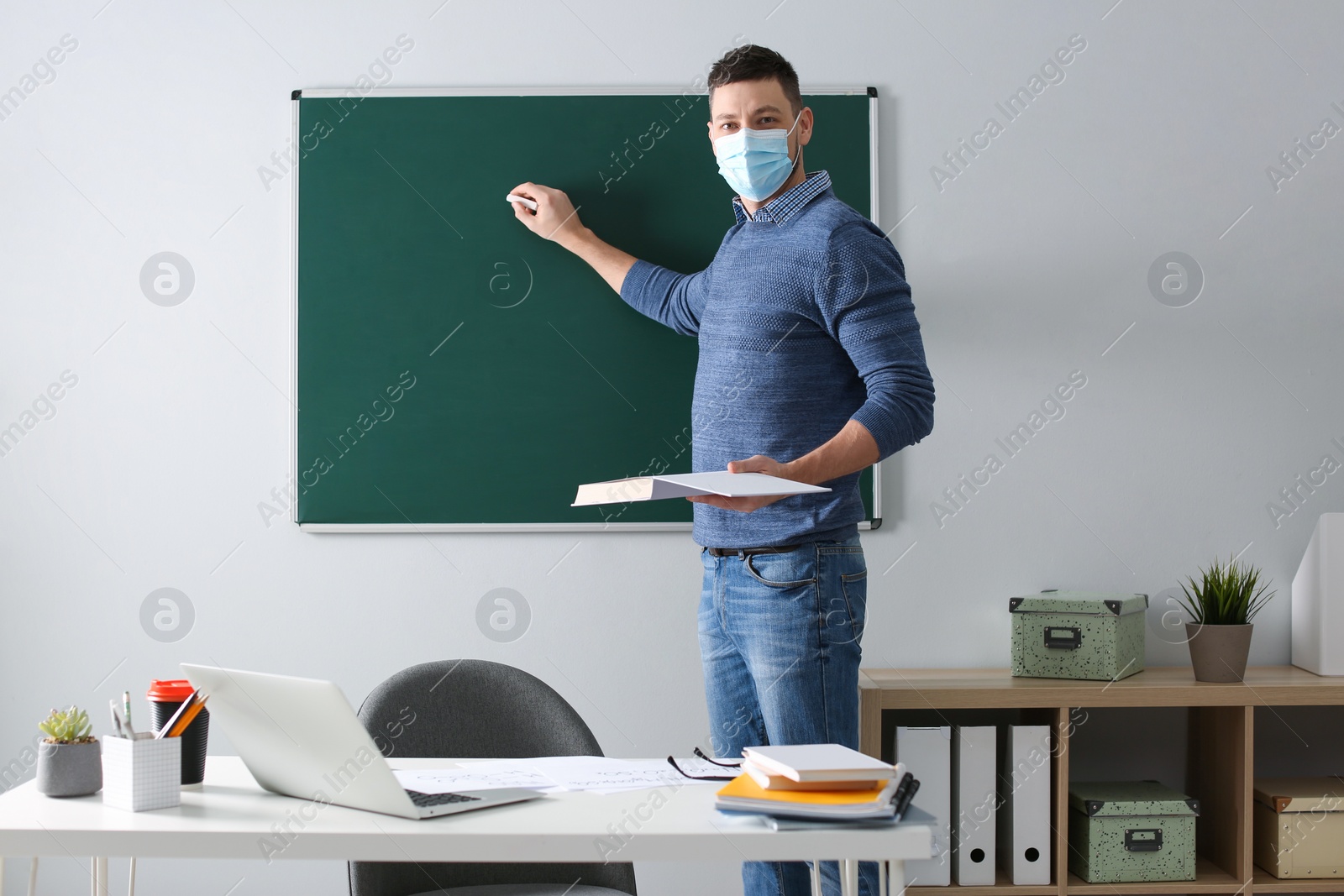 Photo of Teacher with protective mask writing on board in classroom. Reopening after Covid-19 quarantine