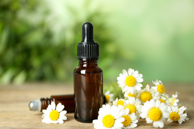 Bottles of essential oil and chamomiles on wooden table