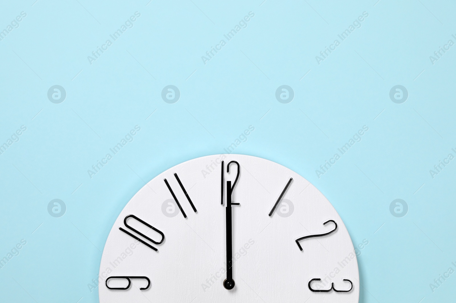 Photo of Stylish analog clock hanging on light blue wall, space for text