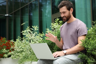 Photo of Handsome man with laptop near beautiful plants on city street