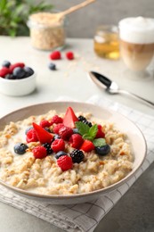 Photo of Bowl of oatmeal porridge served with berries on light grey table