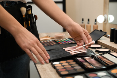 Photo of Professional makeup artist taking brush from bag indoors, closeup