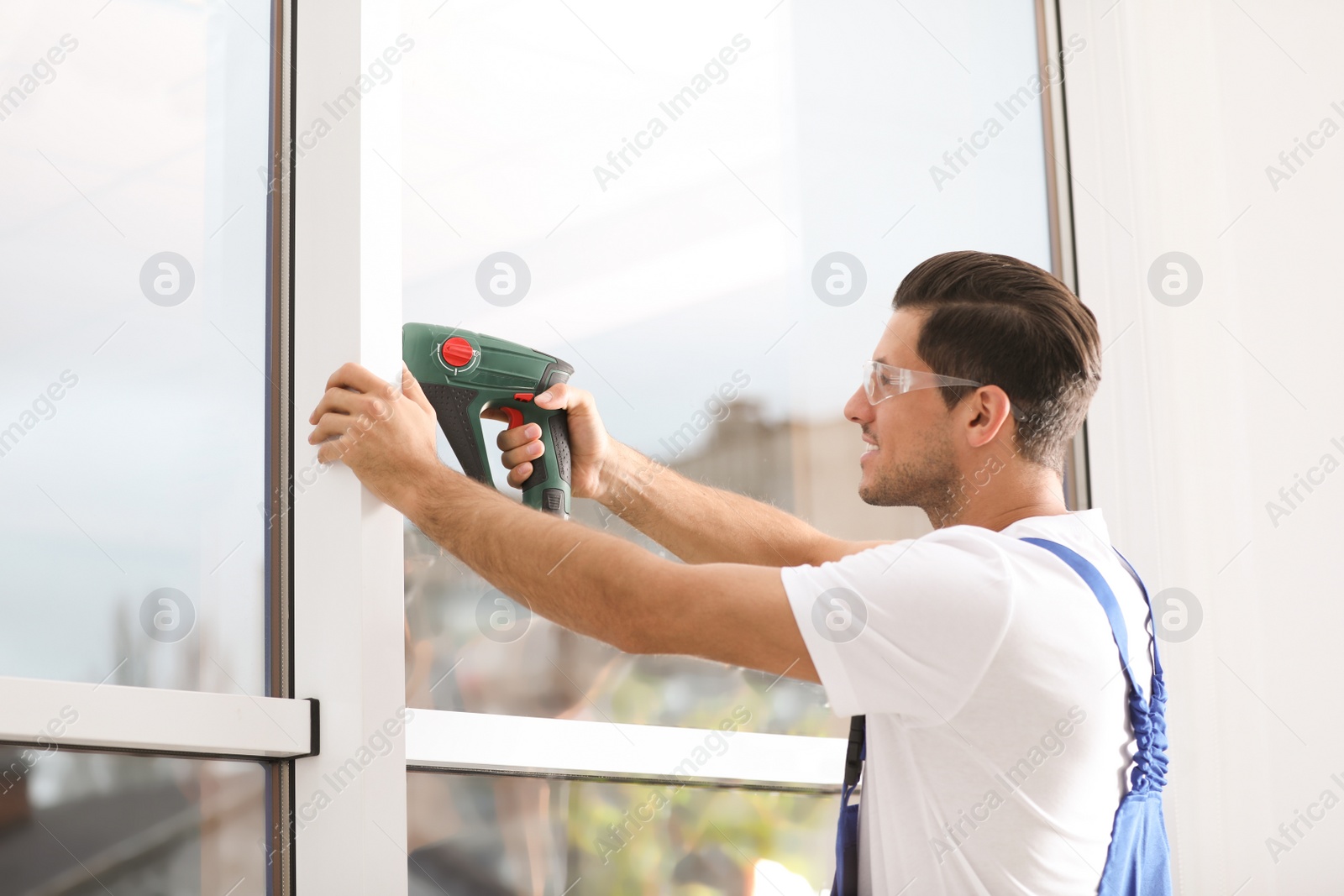 Photo of Construction worker repairing plastic window with electric screwdriver indoors