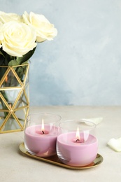 Photo of Burning candles in glass holders and roses on light table, space for text