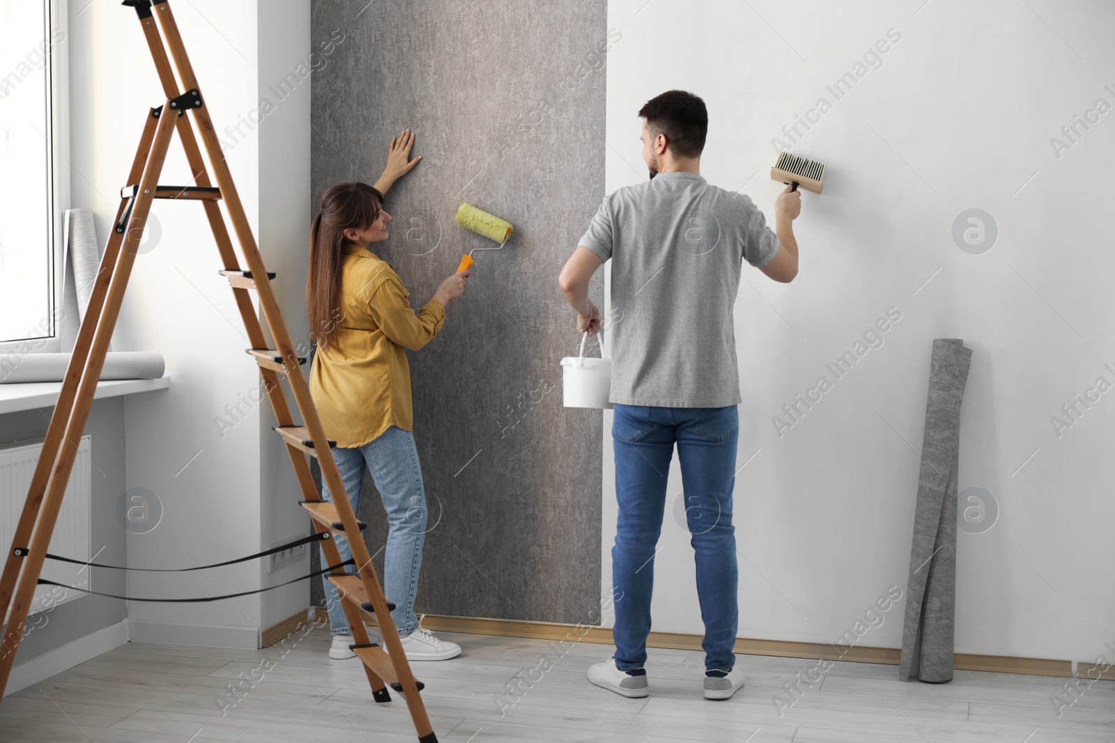 Photo of Woman and man hanging wallpaper in room