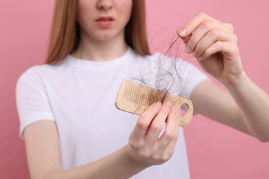 Photo of Woman untangling her lost hair from comb on pink background, closeup. Alopecia problem