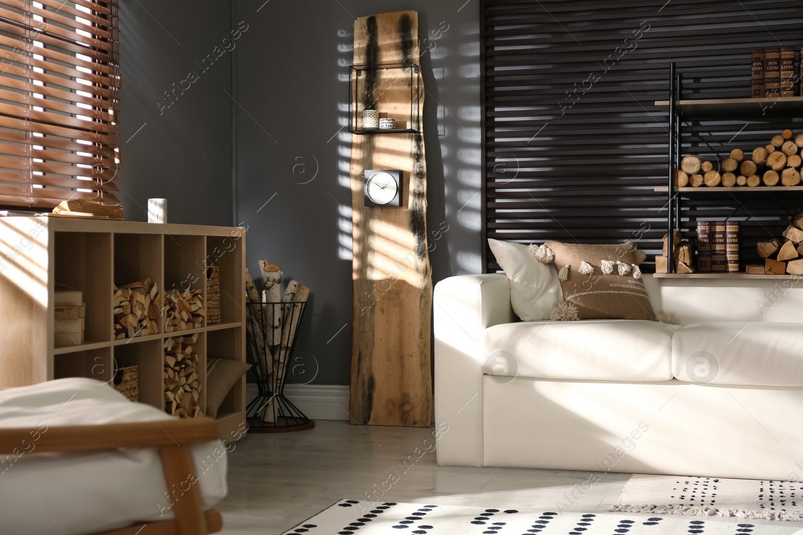 Photo of Shelving unit with stacked firewood and comfortable sofa in stylish room interior