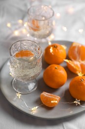 Photo of Delicious ripe tangerines, glasses of sparkling wine and fairy lights on white bedsheet