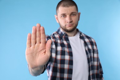 Man showing gesture stop against light blue background, focus on hand