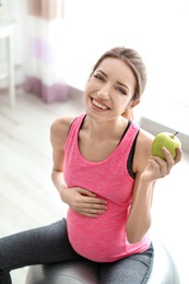 Young pregnant woman holding apple at home