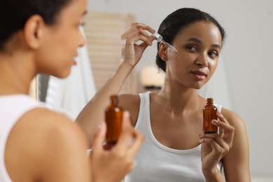 Photo of Beautiful woman applying serum onto her face near mirror in bathroom