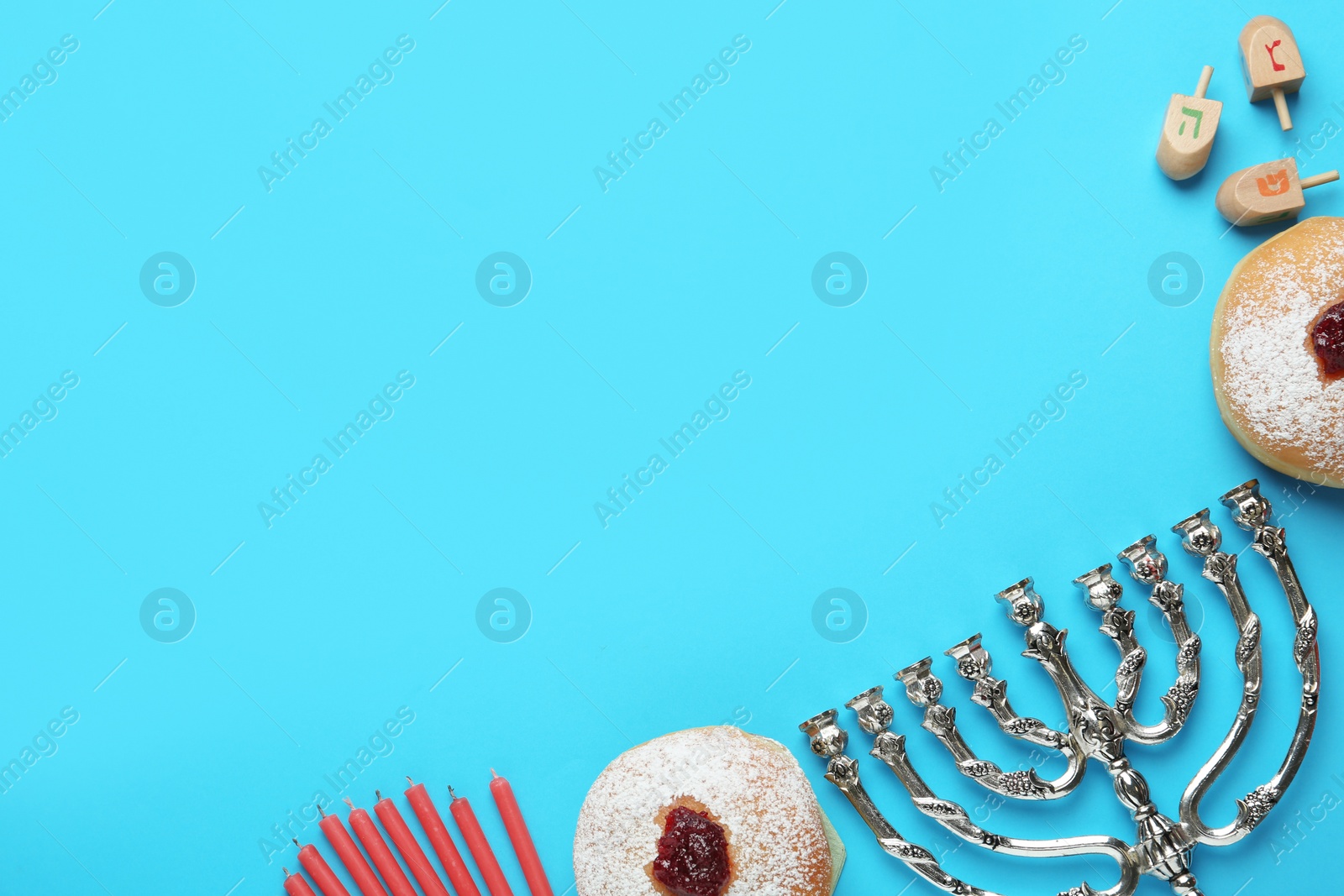 Photo of Hanukkah traditional menorah, candles, doughnuts, dreidels with letters He, Pe, Nun, Gimel on light blue background, flat lay. Space for text