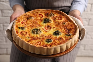 Woman holding delicious homemade vegetable quiche indoors, closeup