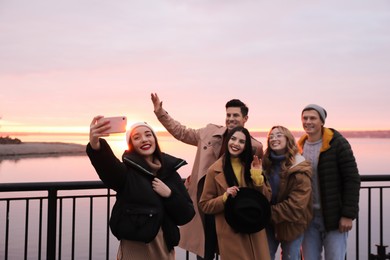 Group of friends making selfie near river at sunset